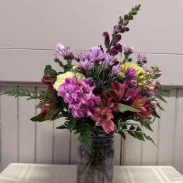 Mixed pink and purple flowers arranged in a glass jar vase