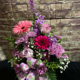 Pink and purple mixed flower arrangement with a floral ribbon bow