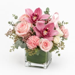 Pink orchids and roses arranged in a clear square vase