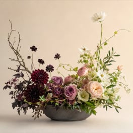 Low floral arrangement in a dark bowl with pink, white, and burgundy blooms