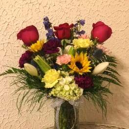 Mixed bouquet of roses, sunflowers, and carnations in a glass vase