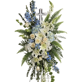 Standing funeral spray with white lilies, cream roses, and blue flowers around a cross