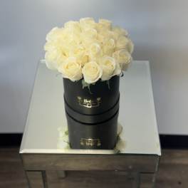 Cream roses arranged in a black round box on a mirrored table