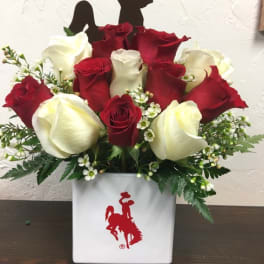 Red and white roses arranged in a white vase with a cowboy silhouette topper