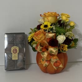 Pumpkin-shaped vase with yellow and orange roses and a chocolate box beside it