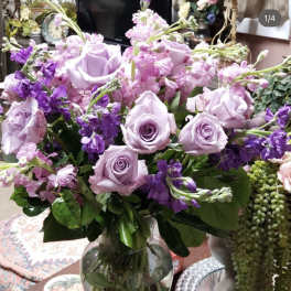 Lavender roses and purple flowers arranged in a clear glass vase