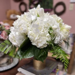 White floral arrangement in a gold vase with green foliage