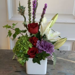 Red roses and white lilies in a white vase with purple spikes and green hydrangea