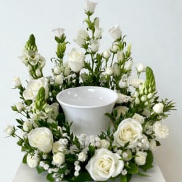 White roses and mixed white flowers arranged around a white urn vase