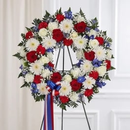 Circular wreath of red, white, and blue flowers on a stand with ribbon