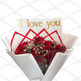 Red roses wrapped in white paper with a gold "I love you" card