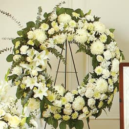 White floral wreath on a stand with lilies and chrysanthemums