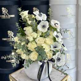 Cream roses and white anemones in a white vase with eucalyptus