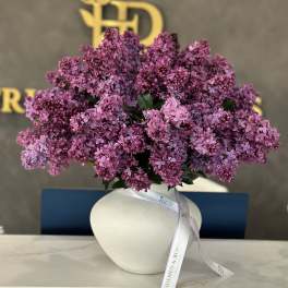 Purple lilac bouquet in a white vase with a ribbon