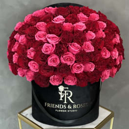 Large round arrangement of pink and red roses in a black hat box