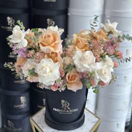 Peach and white roses with small pink flowers in a black hatbox.