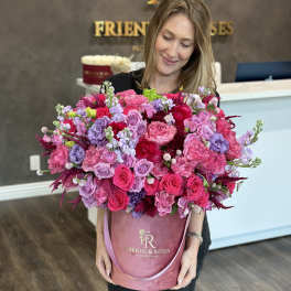 Woman holding a large pink and purple rose arrangement in a velvet hat box