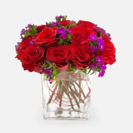 Red roses with purple accent flowers in a clear glass vase