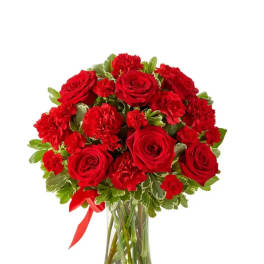 Red roses and carnations in a clear glass vase with a red ribbon