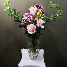 Pink roses and purple daisies in a clear glass vase