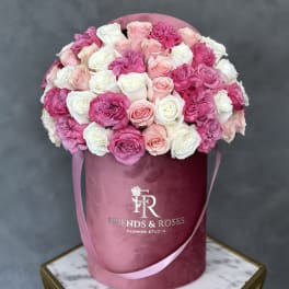 Pink and white roses arranged in a round velvet hat box