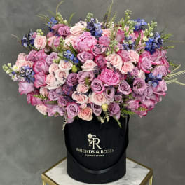 Large bouquet of pink and lavender roses with blue flowers in a black hat box