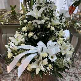 Tall white and cream lily and rose arrangement in a wicker basket with white ribbon bows