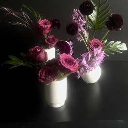 Two floral arrangements in white vases with pink and burgundy blooms
