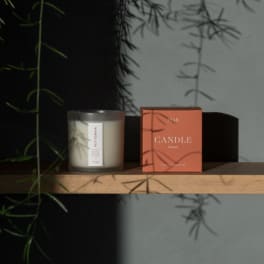 A scented candle in a frosted glass jar beside its coral box