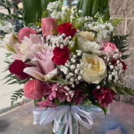Mixed bouquet of pink and white flowers in a glass vase with ribbon