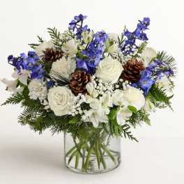 White and blue floral arrangement in a clear glass vase with pinecones