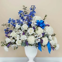 White and blue floral arrangement in a white urn vase with ribbon