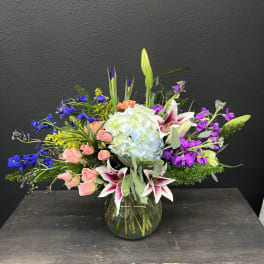 Mixed bouquet in a glass vase with lilies, hydrangea, roses, and purple blooms