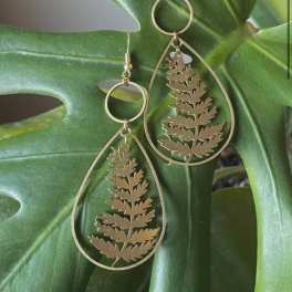 Gold teardrop earrings with fern cutouts on a large green leaf
