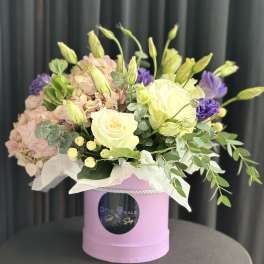 Bouquet of pale pink hydrangeas, white roses, and purple blooms in a pink box