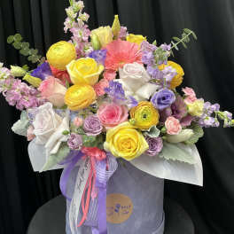 Mixed bouquet of roses, ranunculus, and lisianthus in a round hat box