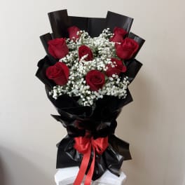 Bouquet of red roses and white baby's breath wrapped in black paper with a red ribbon