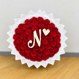 Heart-shaped red rose arrangement with white floral initials and a heart