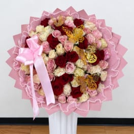 Large bouquet of red, pink, and cream roses with a pink ribbon and butterfly accents