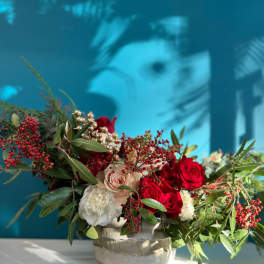 Red and white roses arranged in a low stone vase with berries