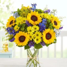 Bouquet of yellow sunflowers and purple flowers in a clear glass vase