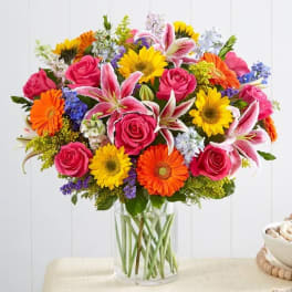 Mixed bouquet of roses, lilies, and daisies in a clear glass vase