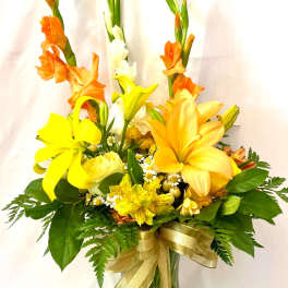 Yellow and orange floral arrangement in a glass vase with a gold ribbon