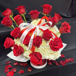 Red roses arranged over white hydrangeas with a ribbon bow