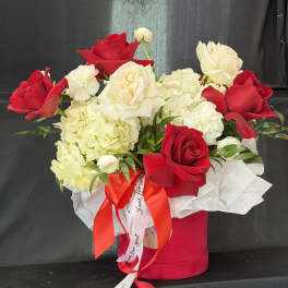 Red and white roses arranged in a pink hat box with a ribbon