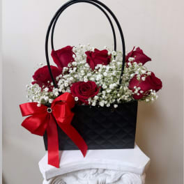 Red roses in a black handled gift bag with a red bow