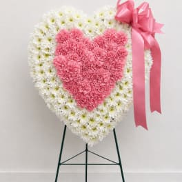 Heart-shaped floral standing spray with pink and white flowers and a pink ribbon