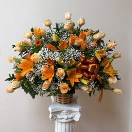 Orange lilies and peach roses in a woven basket on a pedestal
