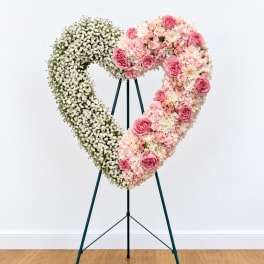 Heart-shaped floral wreath on a stand with pink and white flowers