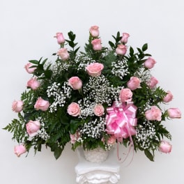 Pink roses arranged in a white basket with a pink ribbon bow